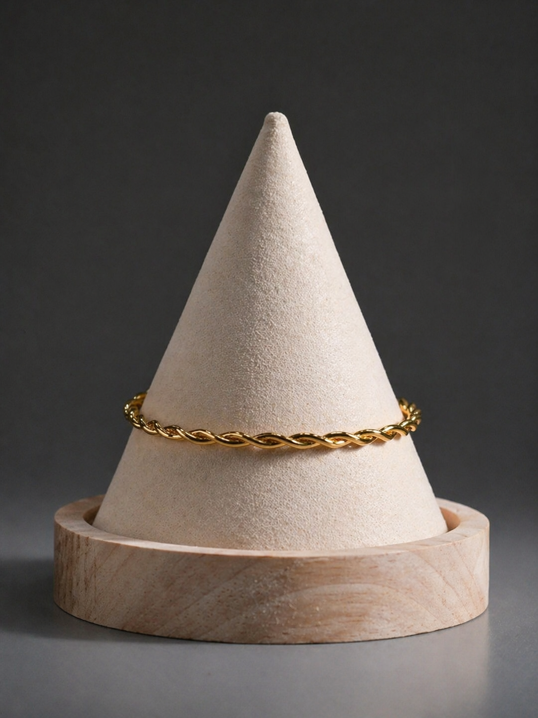 Gold bracelet on a textured cone-shaped object with a wooden base against a dark background