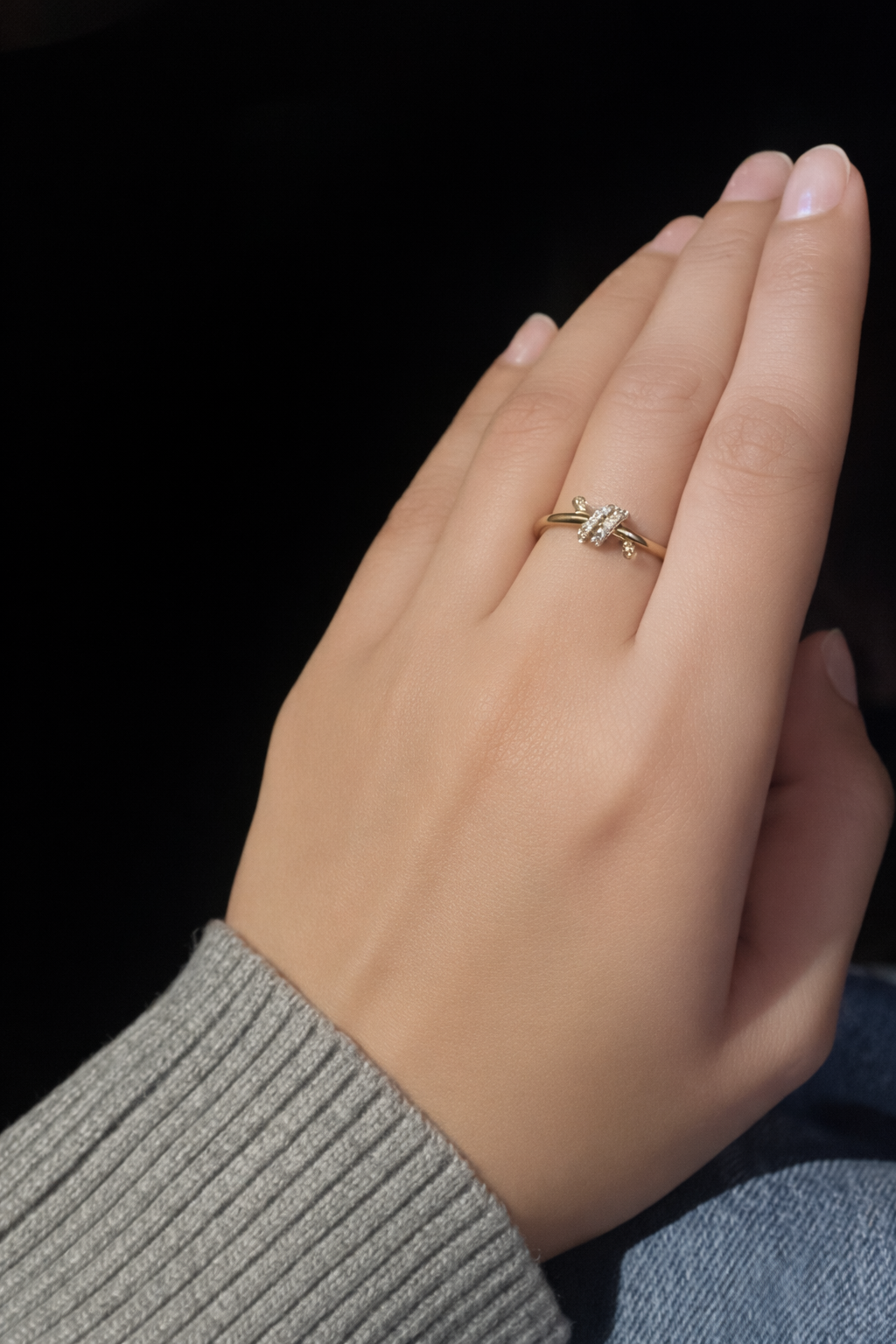 Hand wearing a gold ring with a clear stone against a black background